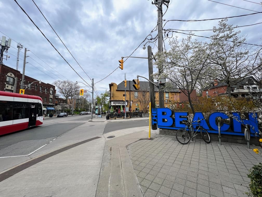View of Queen Street, one of the main streets in the Beaches Neighbourhood. The BEACH sign is visible and the streetcar is travelling along Queen Street.