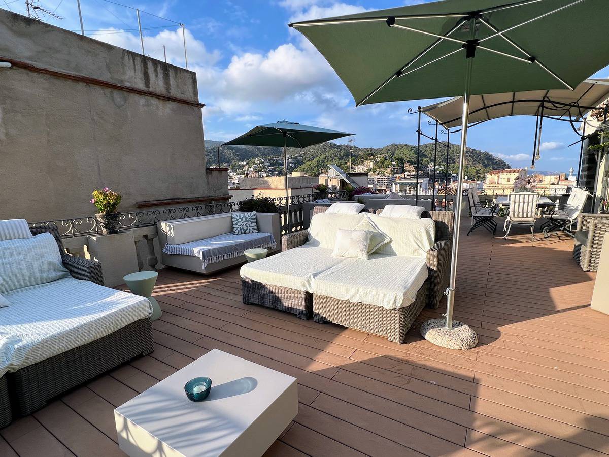 Loungers with umbrellas and coffee tables arranged in comfortable seating on the rooftop terrace of the boutique Tossa de Mar hotel, Casa Granados.
