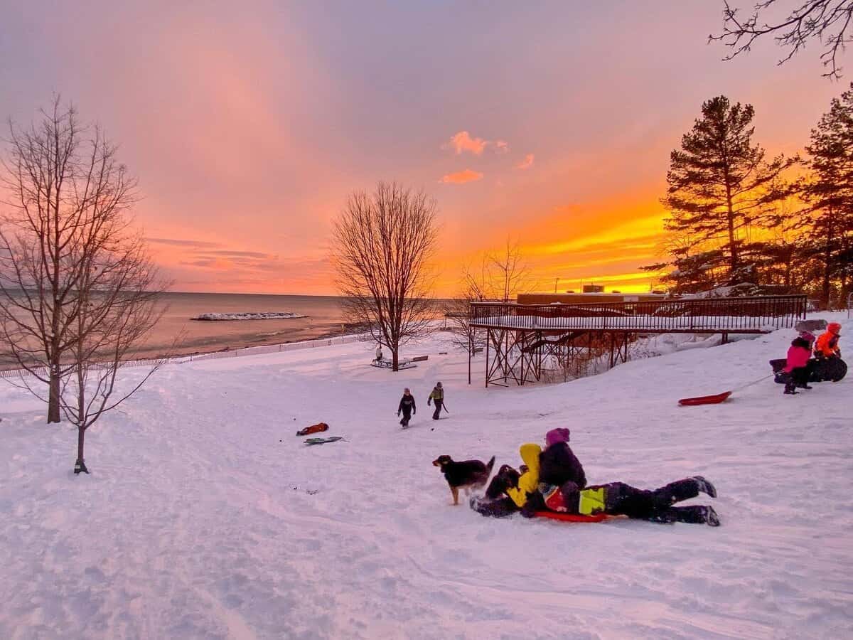 Children sledding near Lake Ontario in Toronto at sunset.