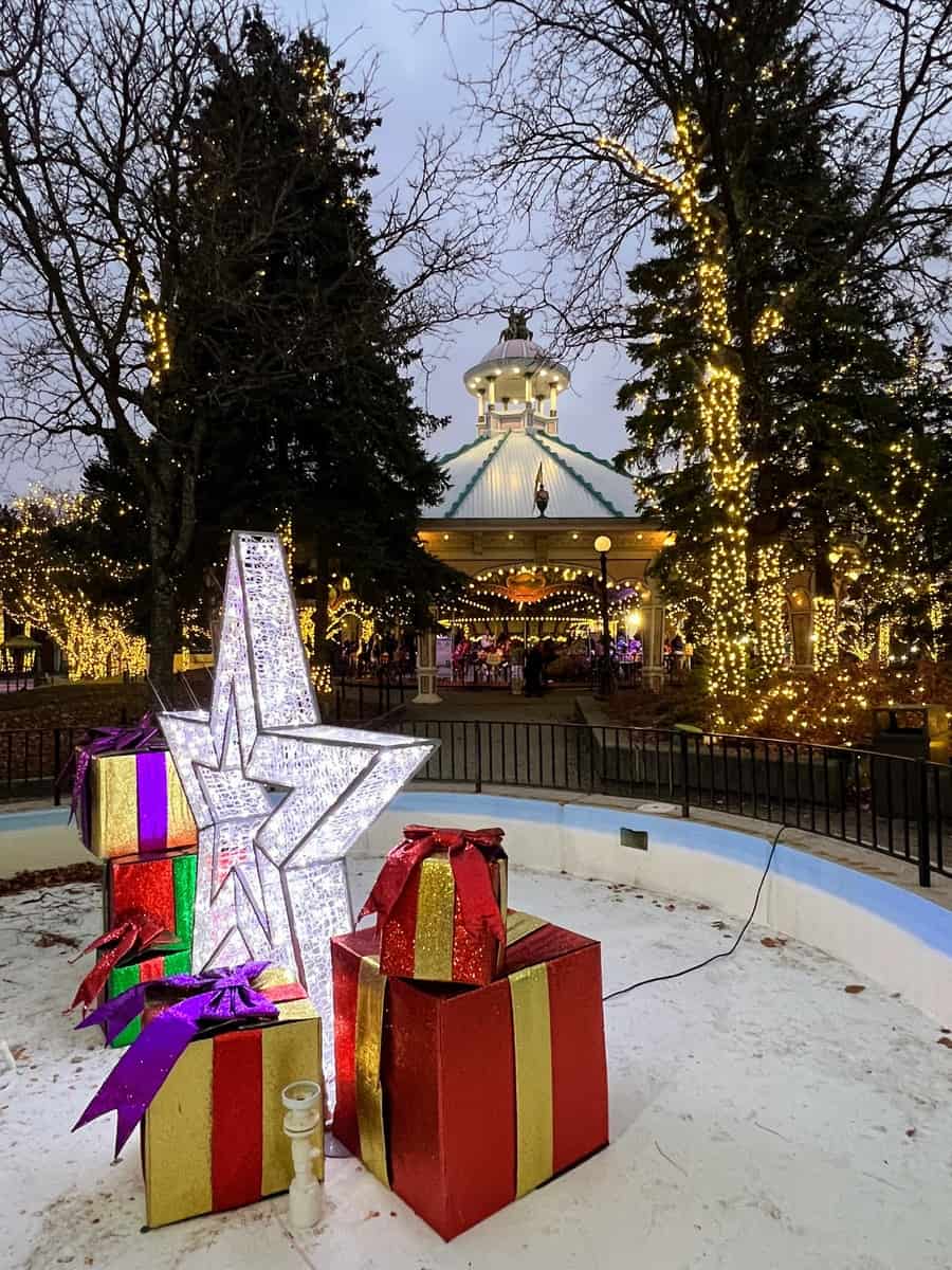 A festive display featuring oversized, brightly coloured gift boxes and a luminous star, set in a winter scene at twilight.