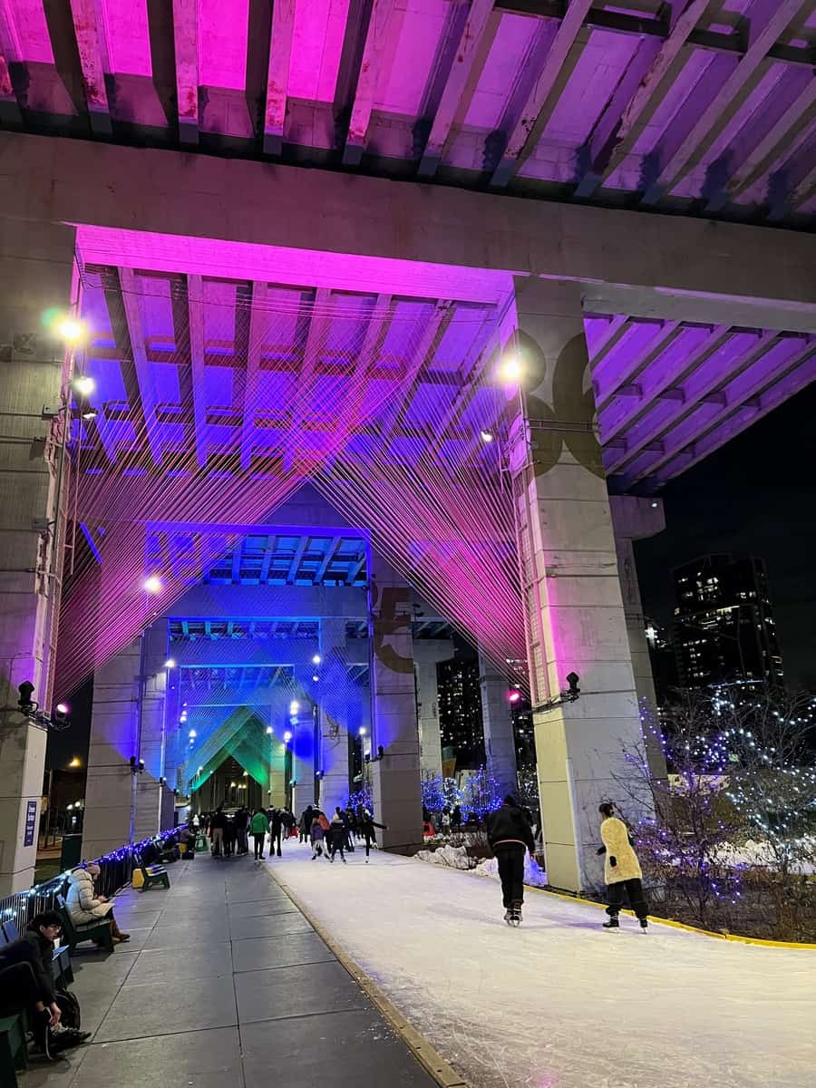 Skaters at the Bentway in Toronto Ontario are ice skating under the projected lights.