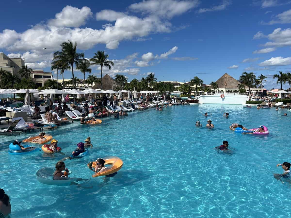 A very busy pool filled with swimmers using floaties. Pool loungers under umbrellas are full with hotel guests at Moon Palace Sunrise.
