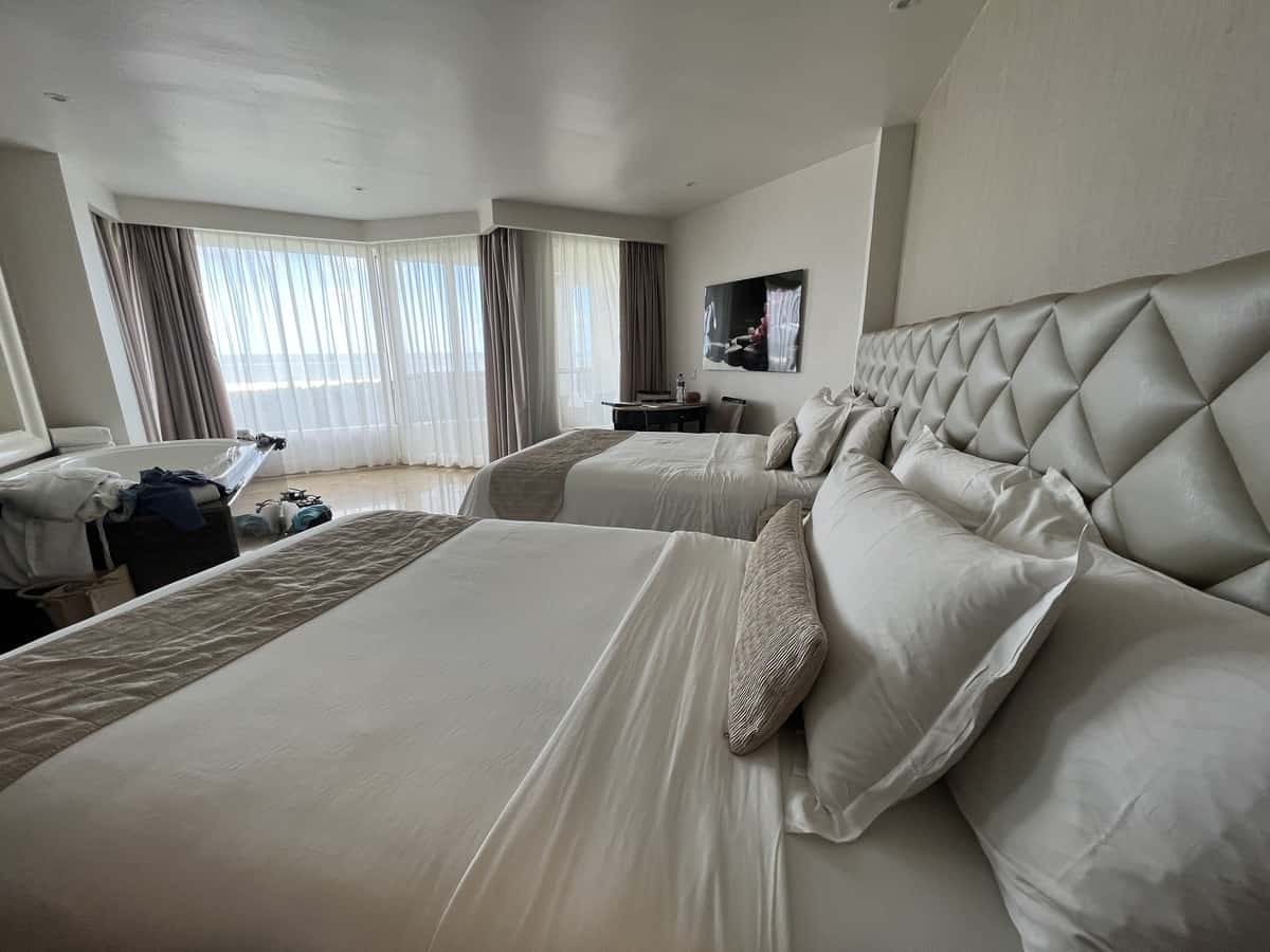 Hotel room with two beds, white bedding, and view of the Caribbean Sea thorugh the windows.