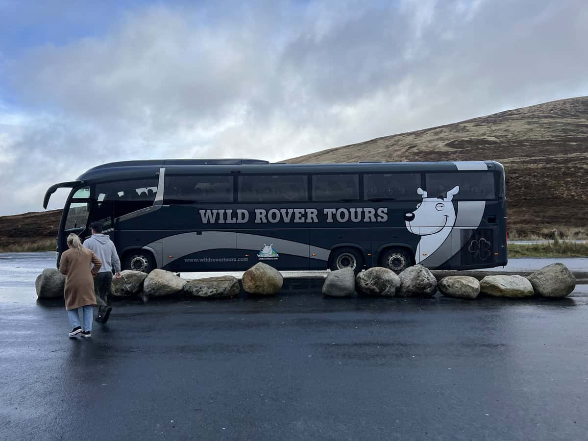A large coach tour bus with the name Wild Rover Tours is pictured in the Wicklow Mountains in Ireland.