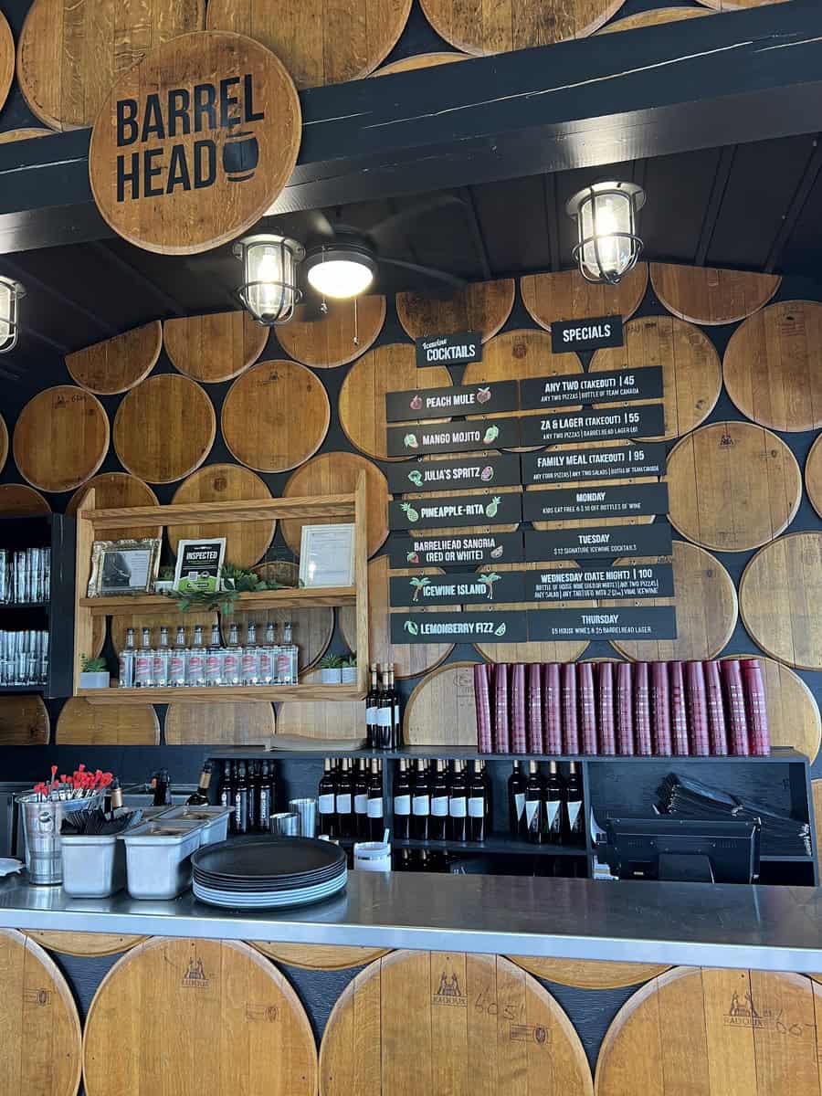 The cozy interior of the "Barrel Head" bar at a notable Niagara on the Lake winery, featuring wooden barrel decor and a menu listing signature cocktails and specials. This venue is a part of the best winery experiences in Niagara on the Lake, offering unique tastes and atmosphere among NOTL wineries.