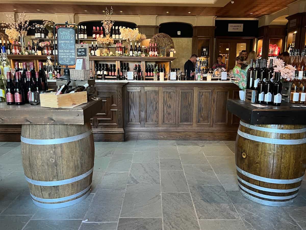 The interior of Reif Estate Winery's tasting room, showcasing wooden barrel tables and a variety of wines on display behind the counter, offering a delightful experience at one of the best wineries in NOTL.
