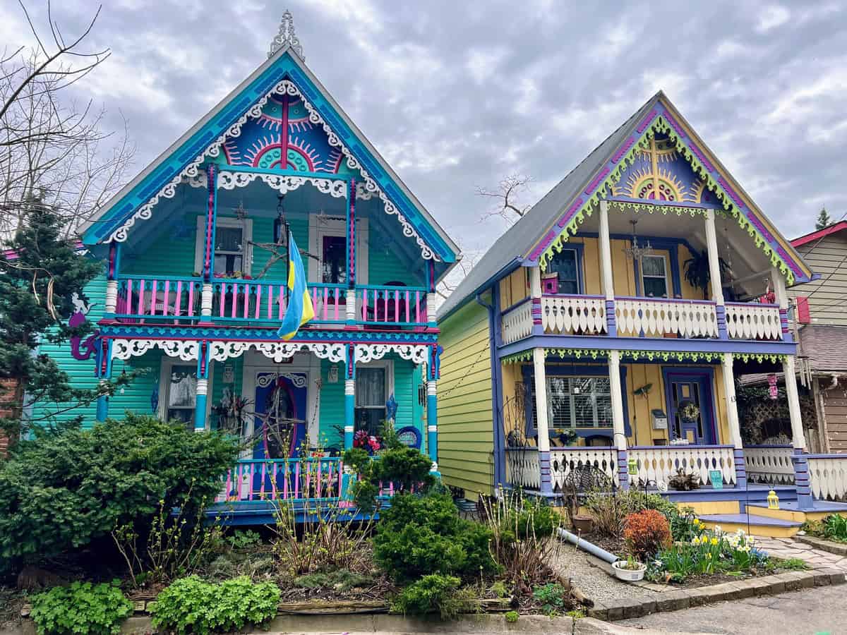 Two vibrant, Victorian-style houses, painted in bright blues, pinks, yellows, and purples, known as "Painted Ladies" in Grimsby, Ontario. Their intricate trim and bold color palettes make these homes a standout architectural attraction.