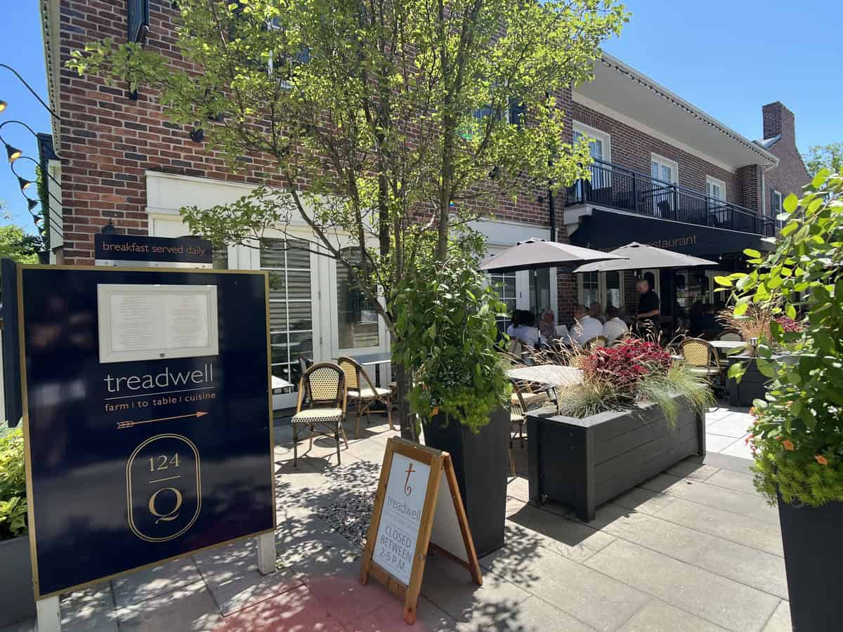 The patio of Treadwell restaurant, shaded by trees and black umbrellas, with an outdoor sign advertising its farm-to-table cuisine. A popular spot for dining in downtown Niagara-on-the-Lake.