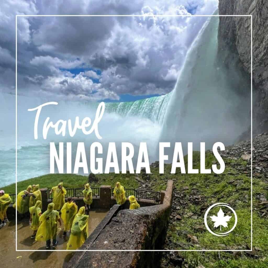 Tourists in yellow rain ponchos stand at a lookout point near the powerful mist of Niagara Falls, with dramatic clouds overhead. Text on the image reads "Travel Niagara Falls," framed with a maple leaf symbol.