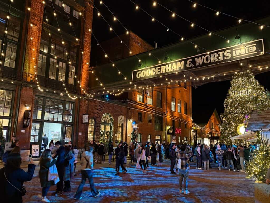 The Distillery District in Toronto during the holiday season, illuminated with festive string lights and a large Christmas tree. Visitors enjoy the vibrant atmosphere, making it one of the top "things to do in Toronto" during winter.