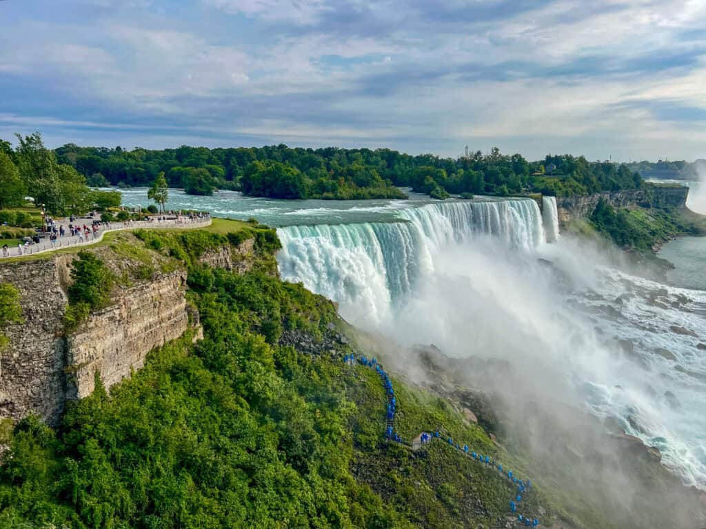 A stunning view of the American Falls at Niagara Falls NY, surrounded by lush greenery and a scenic observation walkway in Niagara State Park. A top attraction near Toronto, perfect for a summer day trip from Toronto, Canada.