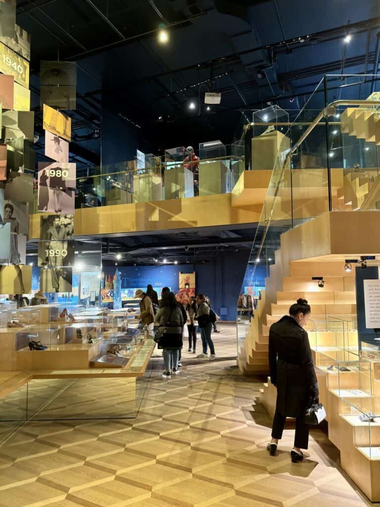 Visitors exploring the modern interior of the Bata Shoe Museum in Toronto, with multi-level wooden staircases, glass display cases, and historical shoe exhibits.