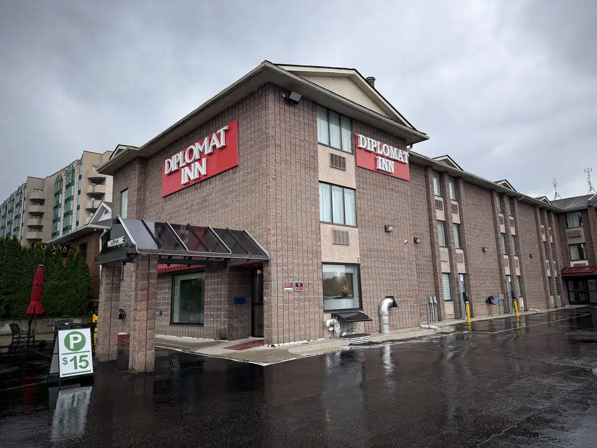 Exterior of the Diplomat Inn in Niagara Falls Canada on a rainy day, featuring a brick building with large red signage and a parking sign at the entrance.