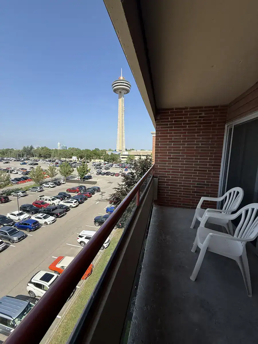 View from the Holiday Inn on the Falls balcony with two white plastic chairs overlooking a large parking lot and the Skylon Tower in Niagara Falls, Canada on a sunny day.