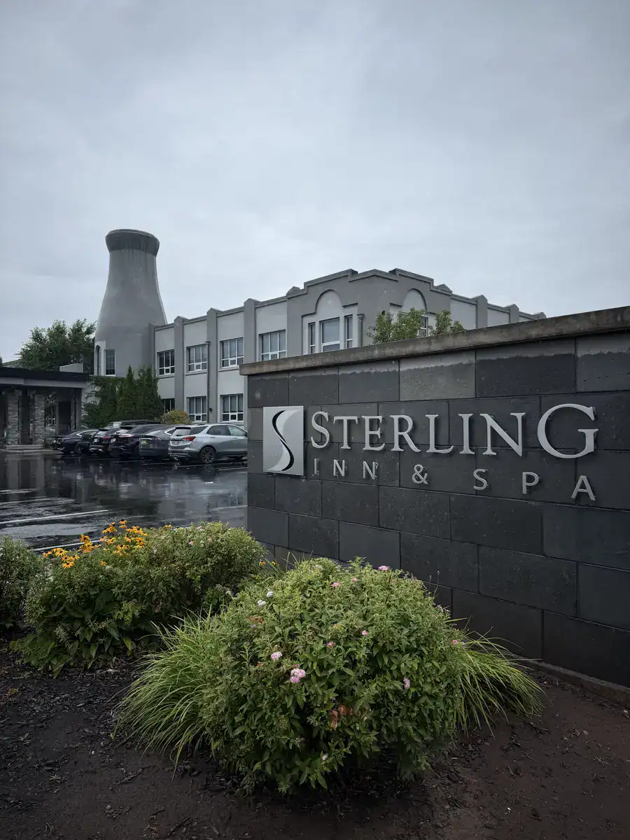 Exterior of Sterling Inn & Spa Hotel in Niagara Falls Canada with its distinctive gray facade and industrial-style tower, set against a cloudy sky with landscaped bushes in the foreground.