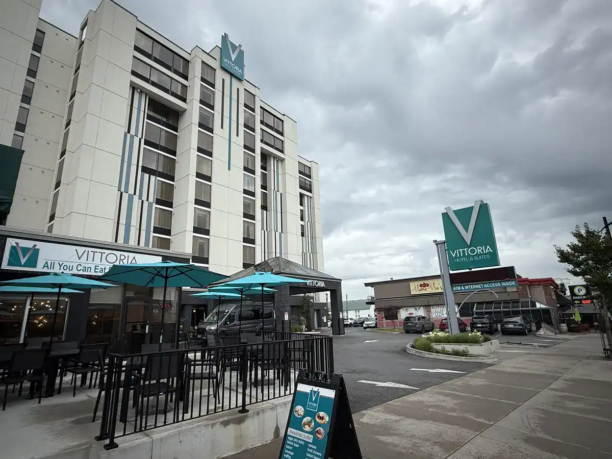 Street view of the budget Vittoria Hotel & Suites in Niagara Falls Canada with its attached all-you-can-eat restaurant and a prominent green hotel sign under a cloudy sky.
