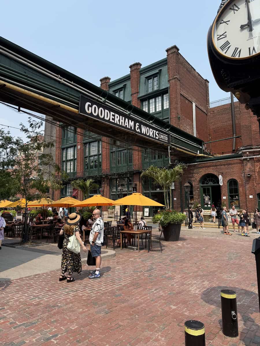 Outdoor summer patio at the Distillery District in Toronto with people dining under bright yellow umbrellas in front of Gooderham & Worts heritage building.