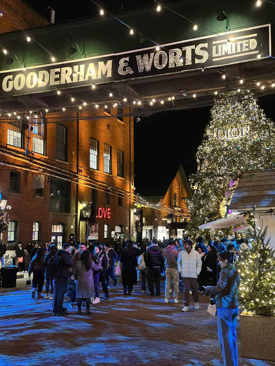 Crowds enjoying the Christmas market at the Distillery District in Toronto under the historic Gooderham & Worts sign and beside the Dior holiday tree.