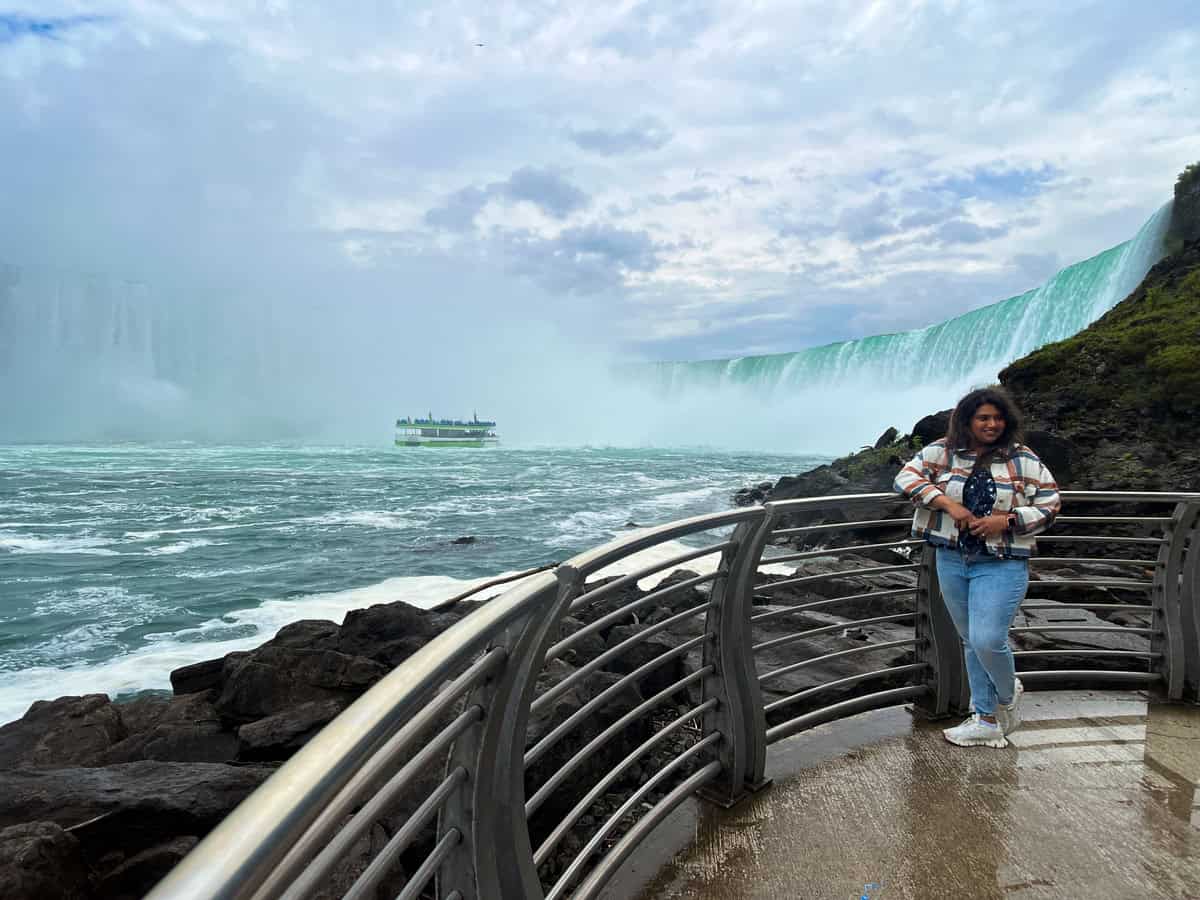 A visitor stands on the Niagara Parks Power Station observation deck with Horseshoe Falls and the Hornblower boat visible behind them.