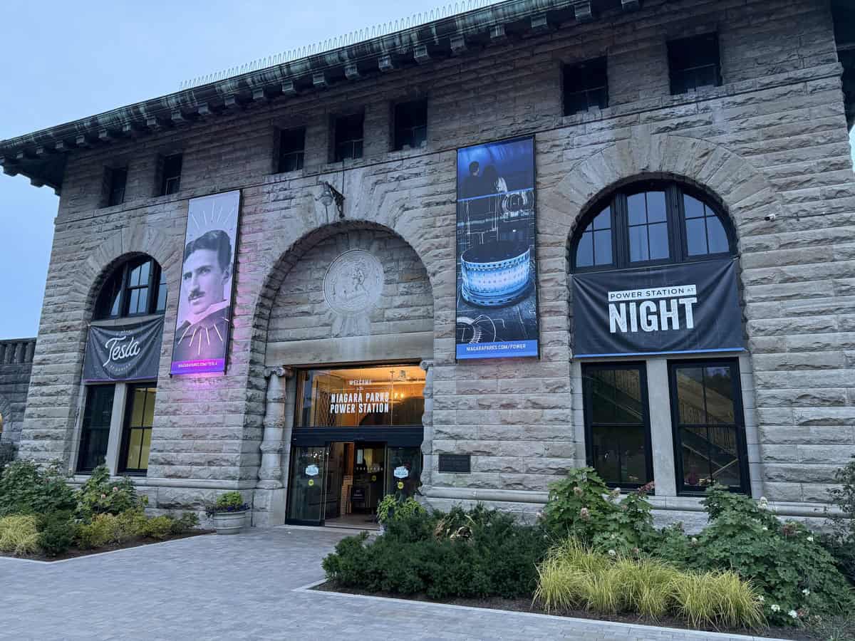 Exterior view of the Niagara Parks Power Station building at twilight, with banners for Tesla and the Power Station at Night exhibit above the entrance.
