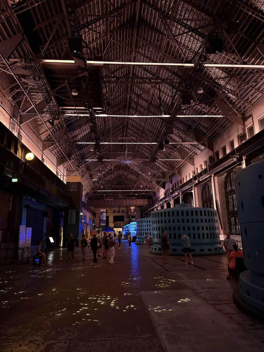 Wide view of the Niagara Parks Power Station generator hall with visitors walking among restored turbines and atmospheric lighting.