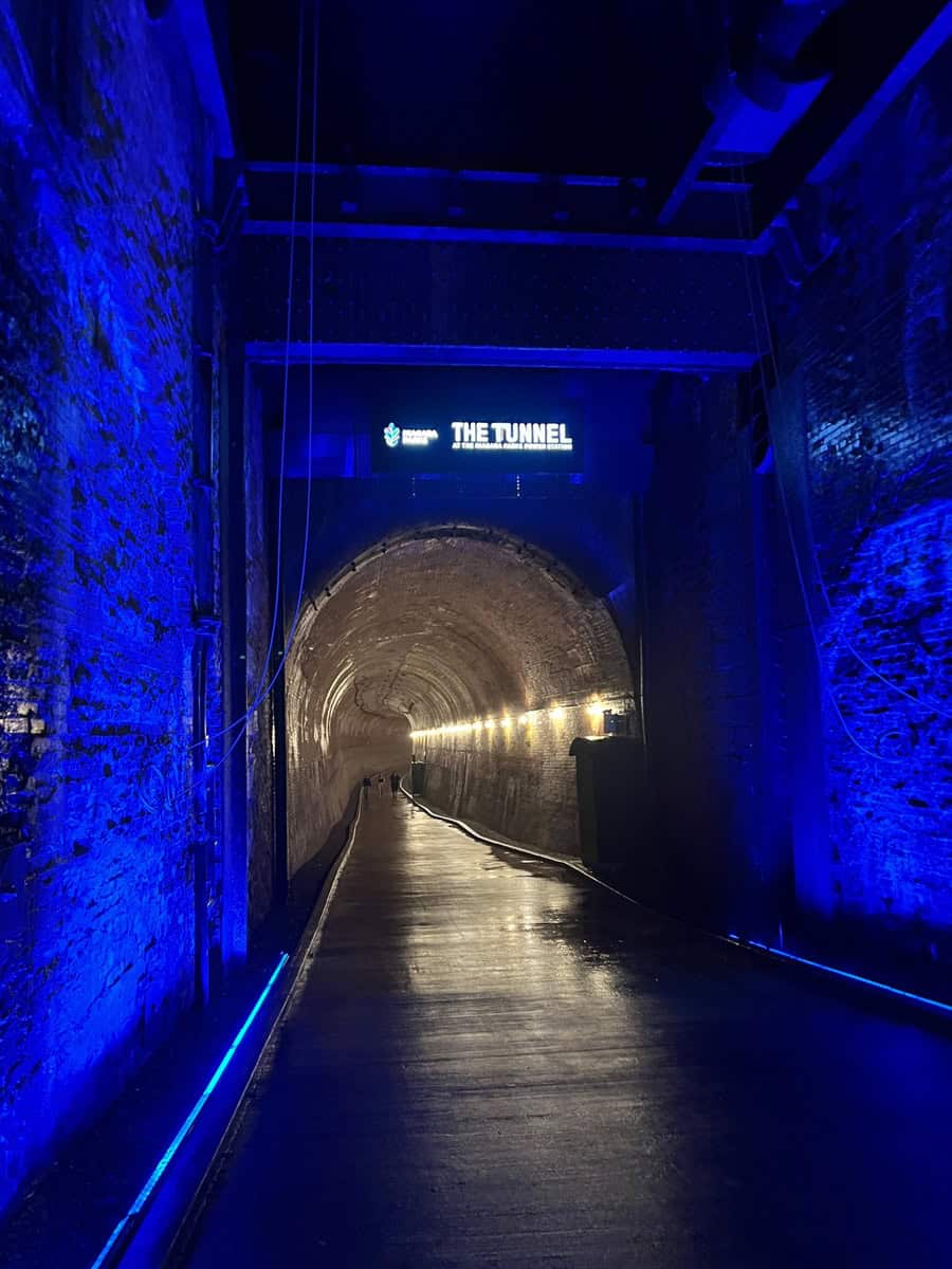 Inside the Niagara Parks Power Station Tunnel, blue lights line the brick walls as visitors walk the long underground passage toward Niagara Falls.