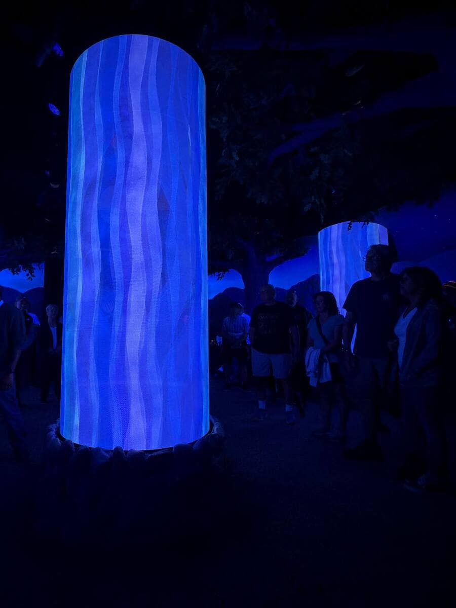 A glowing digital pillar with swirling blue patterns and silhouettes of characters from Indigenous stories, inside the Ancestors Room at Niagara Takes Flight.