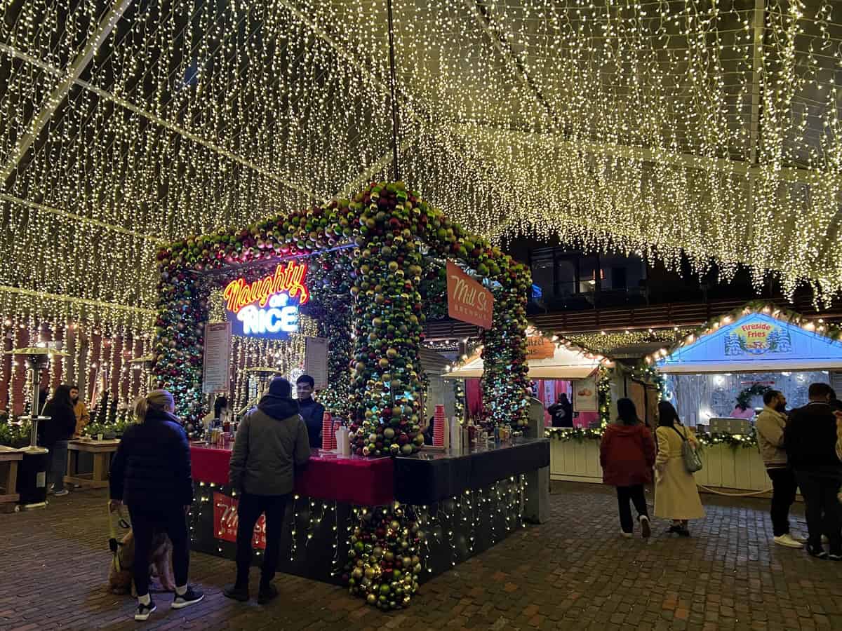 Holiday visitors order drinks at the Naughty or Nice bar surrounded by string lights at the Distillery District winter village in Toronto.