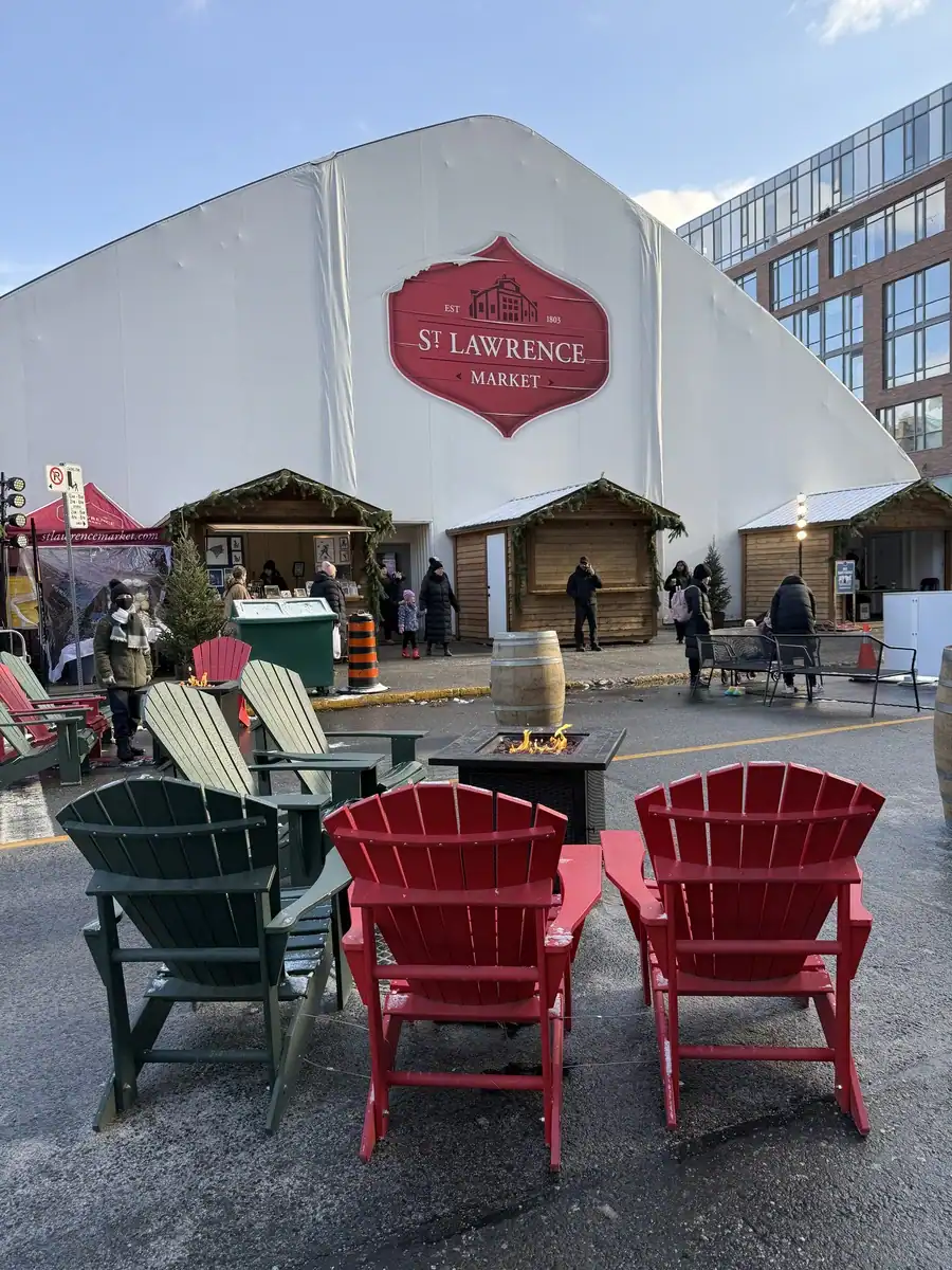 Exterior entrance to Toronto's St. Lawrence Market tent with Muskoka chairs around an outdoor fire pit in winter.