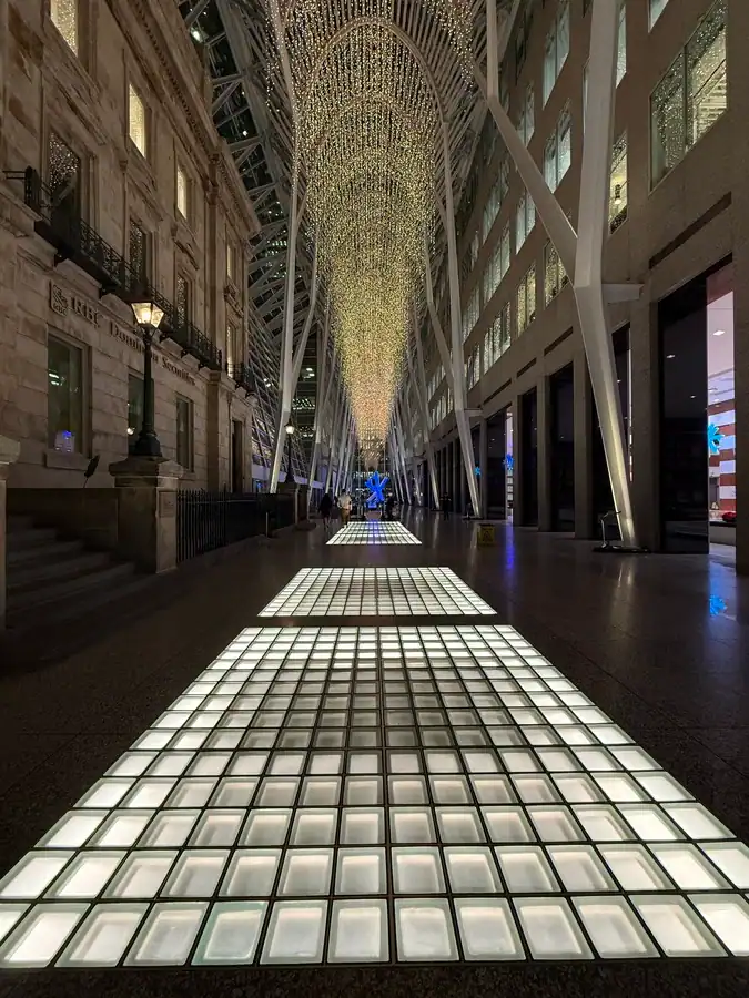 Brookfield Place in Toronto's Financial District is decorated with holiday lights at Christmas. A historic building can be seen on the left while shops are visible on the right.