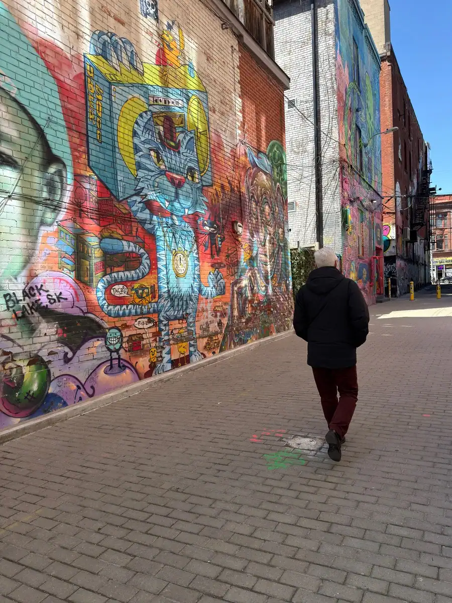 A man walks past bight, colourful graffiti murals in Toronto's graffiti alley.