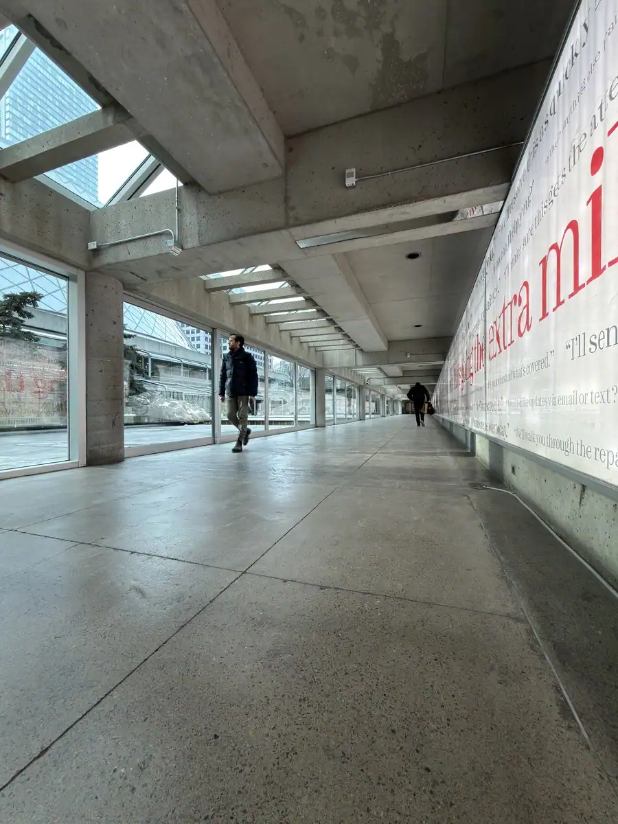 A man walks through the covered walkway with Roy Thompson Hall visible through the large windows. The concrete pathway is part of Toronto's PATH system in downtown.