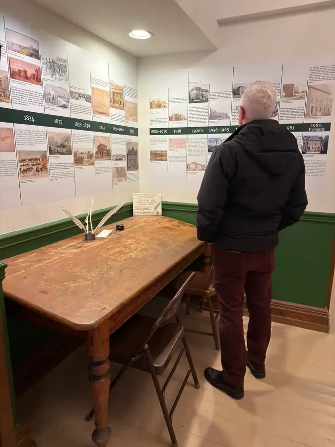 Man reading the historic information posted on the walls of Toronto's First Post Office, a free museum in Toronto. An old desk with quills is in front of the historical display.