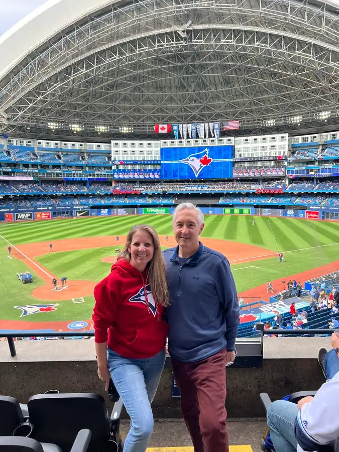 Two fans stand in the 200 level stands at the Rogers Centre in Toronto with the baseball field and Jays logo on display behind the couple.