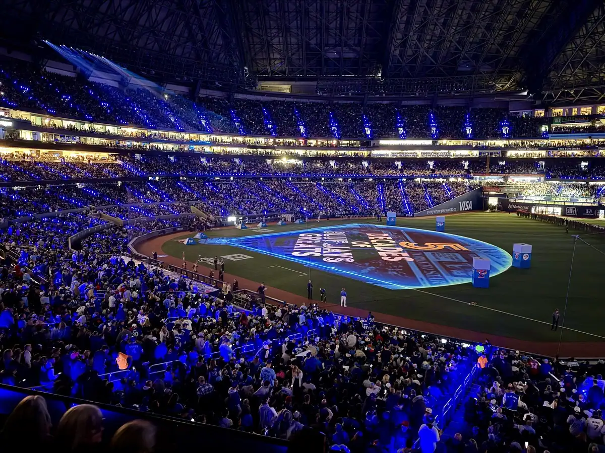 A visual display lights up the field of the Rogers Centre during the Blue Jays' home opener in Toronto. Seats are filled with fans enjoying the show.
