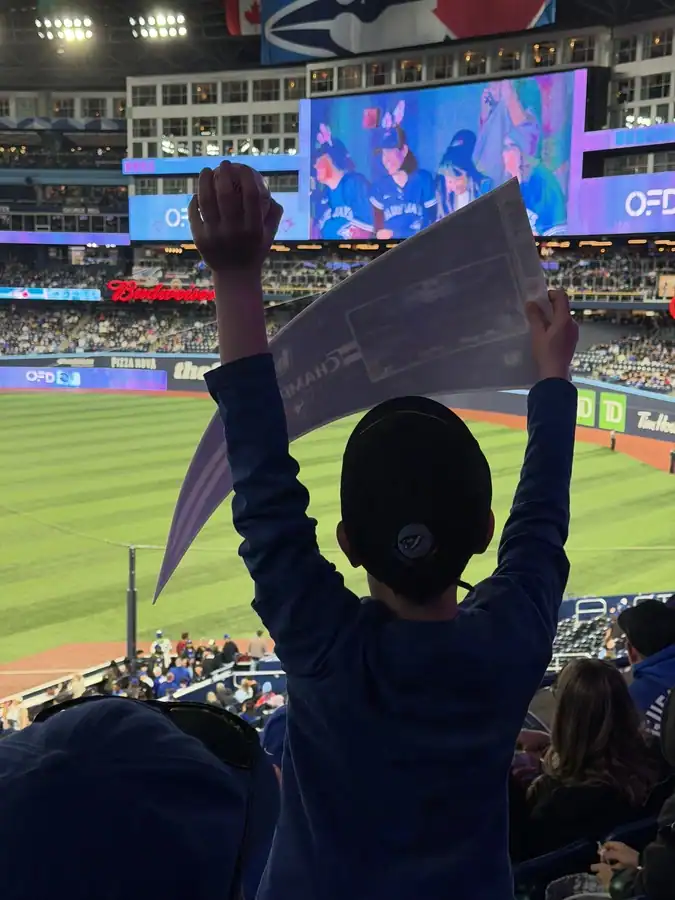 A young Blue Jays fan holds up a pennant and a ball as he cheers on the Blue Jays inside Toronto's Rogers Centre under a closed roof.