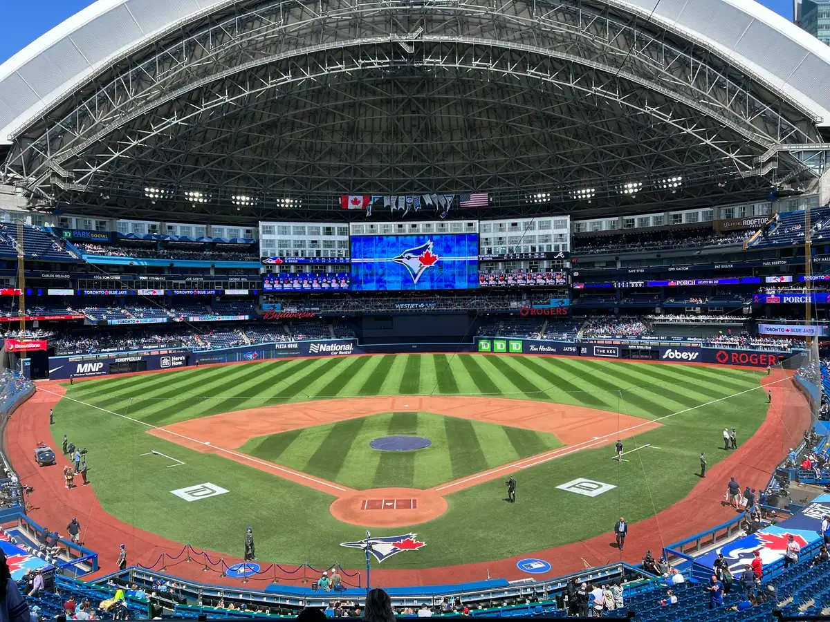 Rogers Centre with the roof open on a summer day overlooking the baseball diamond with the large screen displaying the Toronto Blue Jays logo.
