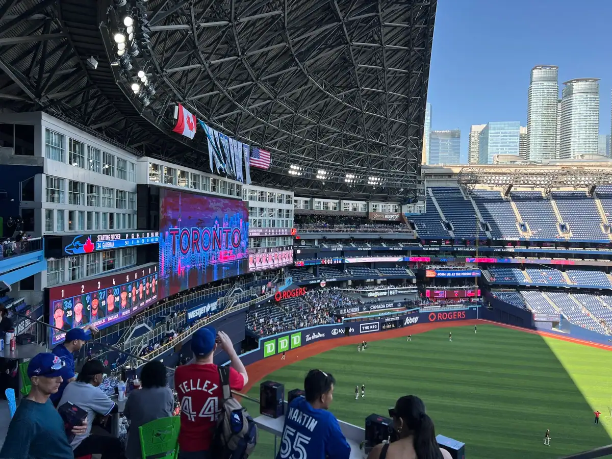 Marriott Hotel rooms overlook the baseball field at the Rogers Centre, home of the Toronto Blue Jays. Fans stand at the roof top bar overlooking the field as players warm up ahead of the game.