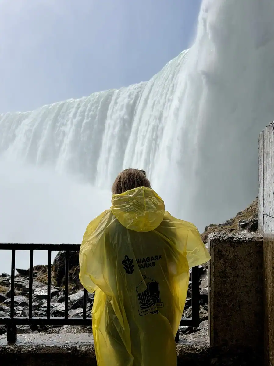 A visitor in a yellow Niagara Parks poncho stands in front of the Horseshoe Falls in Niagara Falls on the observation deck of Journey Behind the Falls.