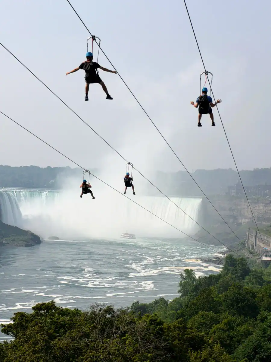 Four riders on the Zipline to the Falls in Niagara Falls Canada heading towards the Horseshoe Falls. The Niagara Boat cruise is at the base of the falls.