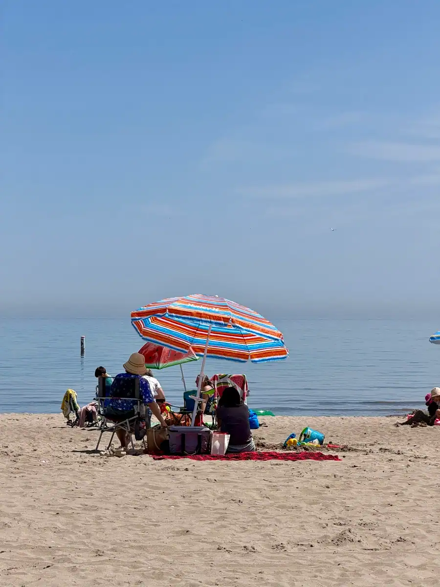 Beachgoers relax beneath a colourful umbrella overlooking calm water of Lake Ontario on the beach at the Scarborough Bluffs.